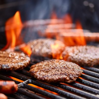 hamburgers and hot dogs cooking on grill with flames