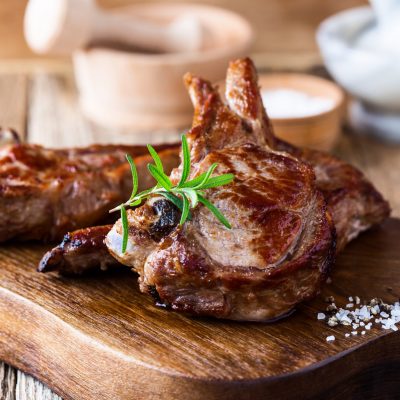 Roasted veal chops with fresh herbs on rustic wooden cutting board, pan seared steak dinner